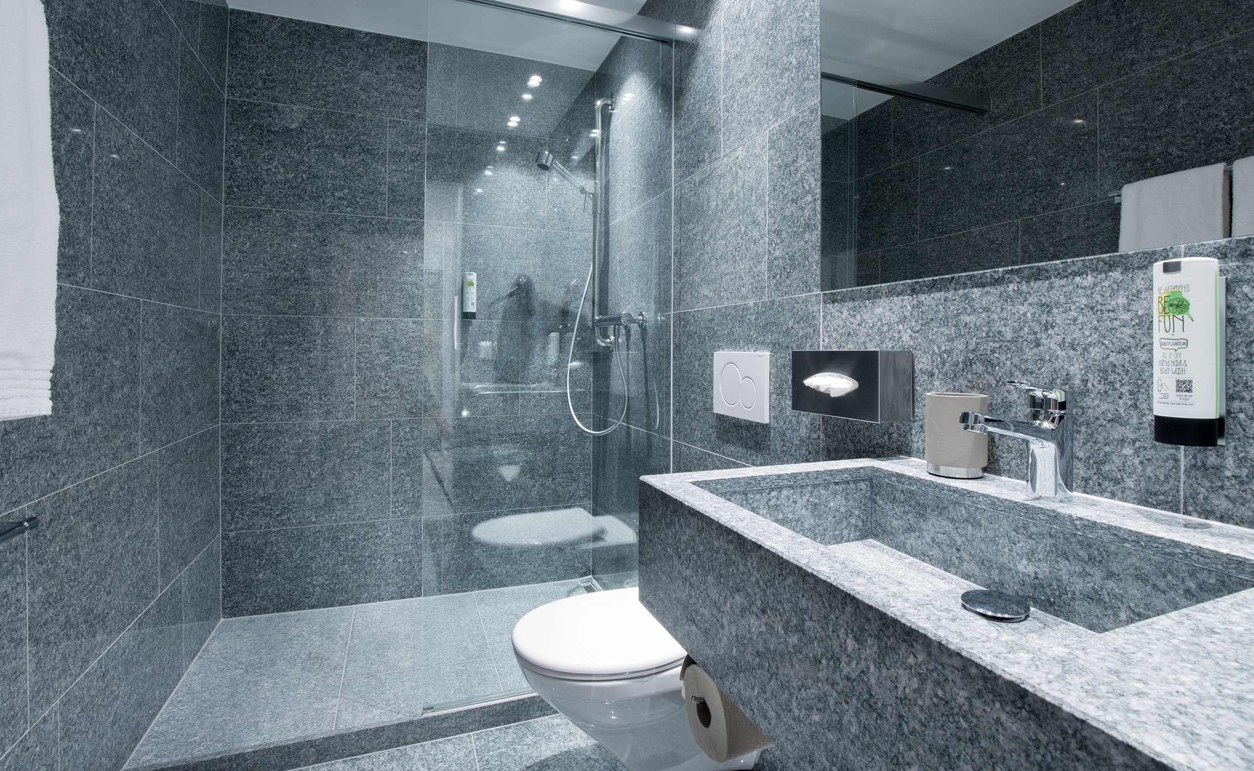 Modern bathroom with gray tiles in Vaduzerhof by B_Smart equipped with shower sink and toilet.